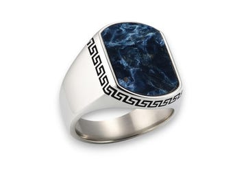 May include: A silver ring with a rectangular, dark blue stone. The ring features a Greek key design on the sides and around the stone. The stone has a marbled appearance with shades of blue and white.