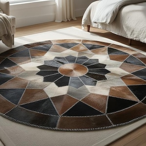 May include: A round rug with a geometric pattern in shades of brown, black, gray, and cream. The rug is made of stitched together pieces of hide, creating a unique and textured surface. The rug is approximately 7 feet in diameter.