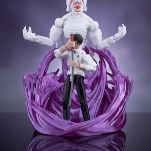 May include: A white action figure of a large, monstrous figure with a wide, toothy grin and multiple arms, standing over a smaller figure holding a sword. The figures are set against a purple background.