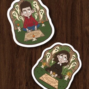 May include: Two die-cut stickers with illustrations of people using Ouija boards. One sticker shows a person in a red hoodie, the other in a black dress. Both are surrounded by ghosts and candles. The Ouija boards have the alphabet, numbers, and the word "Ouija" printed on them.