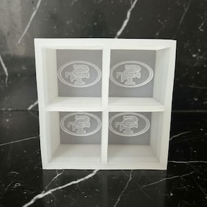 May include: A white, four-compartment shelf featuring the San Francisco 49ers logo etched into each section. The logo is a stylized SF with a football shape. The shelf is made of a translucent material.