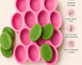 Puede incluir: Molde de silicona rosa con cavidades ovaladas, que contiene jabones ovalados verdes. El molde tiene el texto "SILICONE MOLD" y "High-Quality Silicone". Las dimensiones son 8,9 cm x 6,4 cm con un grosor de 2,5 cm. Los jabones están etiquetados "OSCAR LES VACANCES".