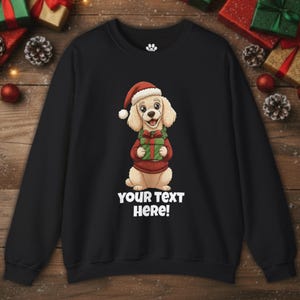 May include: Black sweatshirt with a cartoon dog wearing a Santa hat and holding a gift. The dog is wearing a red sweater. The text "YOUR TEXT HERE!" is printed in white below the dog.