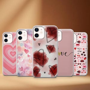 Pode incluir: Uma coleção de cinco capas de telemóvel com vários designs com tema de coração. As capas apresentam corações rosa e vermelhos, efeitos de aquarela e a palavra "love". As capas são projetadas para um smartphone.