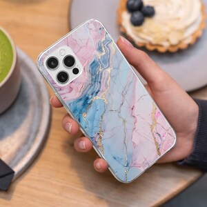 K&ouml;nnte beinhalten: Eine Smartphone-H&uuml;lle mit Marmordesign in Rosa-, Blau- und Goldt&ouml;nen. Die H&uuml;lle hat einen transparenten Rand und einen Kameraausschnitt. Das Marmormuster weist flie&szlig;ende Farbadern und goldene Akzente auf.