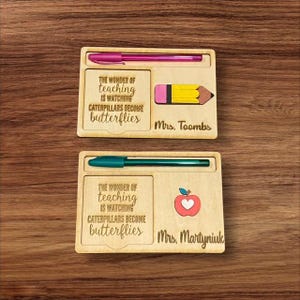Puede incluir: Dos regalos de madera para el aprecio de los maestros con un portaplumas, un pequeño espacio para un lápiz u otro objeto pequeño, y un espacio para un mensaje personalizado. El regalo superior tiene un lápiz amarillo y el texto "THE WONDER OF teaching IS WATCHING CATERPILLARS BECOME butterflies Mrs. Toombs". El regalo inferior tiene una manzana roja con un corazón blanco y el texto "THE WONDER OF teaching IS WATCHING CATERPILLARS BECOME butterflies Mrs. Martyniuk".