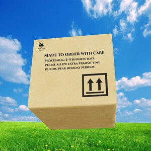 May include: A tan cardboard shipping box featuring a black swan logo and the text MADE TO ORDER WITH CARE, PROCESSING: 2-5 BUSINESS DAYS, PLEASE ALLOW EXTRA TRANSIT TIME DURING PEAK HOLIDAY PERIODS, and a black upward-pointing arrow symbol.