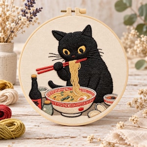 Puede incluir: Un bastidor de bordado circular que contiene un diseño cosido a mano de un gato negro con grandes ojos amarillos comiendo fideos de un cuenco blanco con patrones rojos usando palillos rojos. La escena incluye una botella y platos.