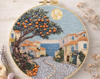 May include: Embroidered landscape scene in a wooden hoop. The artwork depicts a coastal village with a cobblestone street, orange trees, and buildings with orange tile roofs. A full moon is in the sky. The embroidery uses various shades of blue, orange, and beige.