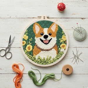 Può includere: Ricamo a cerchio con cane corgi. Il corgi ha pelo marrone e bianco, un viso sorridente ed è circondato da fiori gialli e fogliame verde. Il ricamo è in un telaio di legno. Sono visibili anche forbici, filo e spilli.