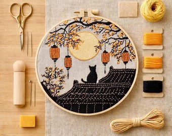 May include: An embroidery hoop featuring a black cat silhouette sitting on a tiled roof under a large yellow moon and hanging lanterns. The kit includes gold scissors, a wooden tool, needles, a yellow wax block, and spools of yellow, orange, and black thread.
