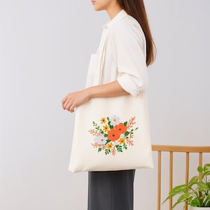 Peut inclure: Sac fourre-tout crème avec un motif floral composé de fleurs orange, jaunes, blanches et vertes. Le sac est porté à l'épaule et présente un design simple et minimaliste, adapté à un usage quotidien.