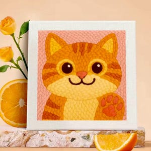 Peut inclure: Une toile carrée représentant un chat tabby orange souriant avec de grands yeux et une patte levée. Le chat est placé sur un fond rose et encadré d'une bordure blanche. L'image est accompagnée de roses oranges et d'une tranche d'orange.