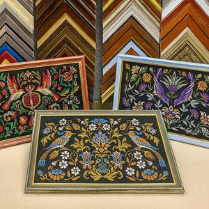 Puede incluir: Tres obras bordadas enmarcadas con intrincados diseños florales y de aves. Los marcos son de varios colores, incluyendo rojo, azul y verde. La obra presenta un fondo negro con detalles de hilo colorido.