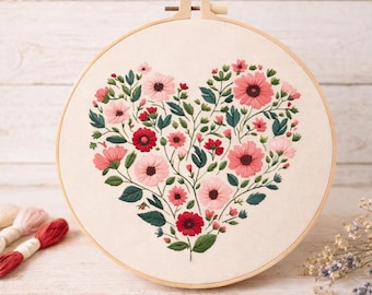 May include: A heart-shaped embroidery hoop featuring a floral design. The design includes pink and red flowers with green leaves, set against a cream-colored fabric. The wooden hoop is visible, and embroidery floss is in the background.