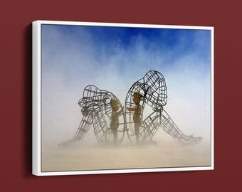 Puede incluir: Obra de arte enmarcada que presenta dos figuras humanas de alambre en posición sentada, sobre un fondo brumoso de color claro y un cielo azul. Las figuras están construidas con líneas de metal oscuro, creando una apariencia de jaula.
