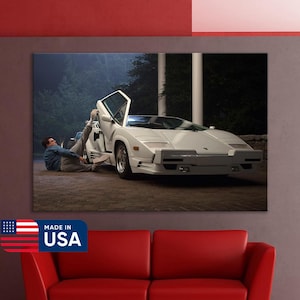May include: A framed canvas print showing a white Lamborghini sports car with an open door. A person is leaning against the car. The print is displayed above a red sofa. The words "Made in USA" are printed on the bottom left.
