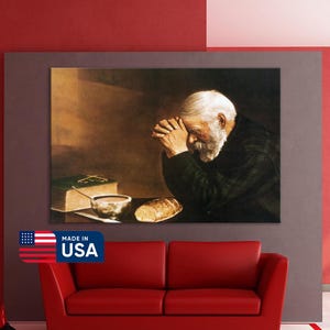 May include: A framed canvas print of an elderly man with a white beard, hands clasped in prayer. A book, bowl, and bread are on the table. The print is above a red sofa. The words "MADE IN USA" are on a sticker.