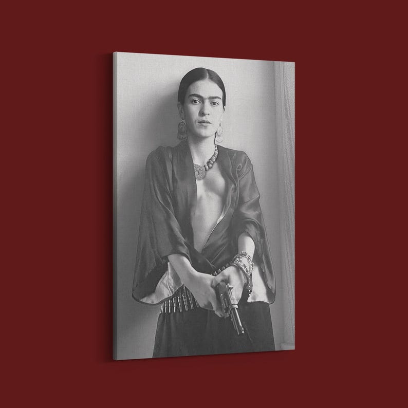 May include: Black and white portrait print of a woman in a dark robe, holding a gun. She wears a necklace, earrings, and bracelets. The image is a canvas print, leaning against a wall.