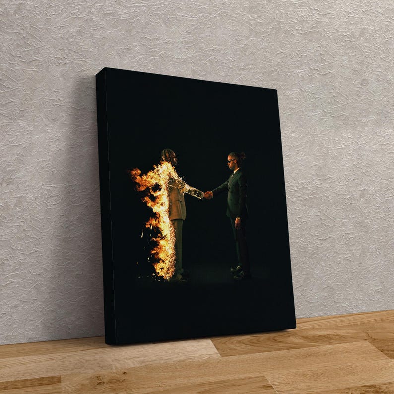 Puede incluir: Impresi&oacute;n en lienzo enmarcada que muestra a dos figuras d&aacute;ndose la mano sobre un fondo negro. Una figura est&aacute; en llamas, la otra con un traje verde oscuro. La obra de arte se exhibe sobre una superficie de madera.