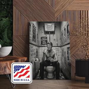 Peut inclure: Impression en noir et blanc d'un homme assis sur des toilettes, tenant un verre et faisant un geste obsc&egrave;ne. Le mur est orn&eacute; d'affiches et de l'inscription "SPACE ODDITY TOILET" et "ZIGGY STARDUST WAS HERE".