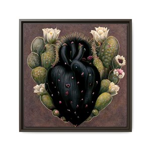 May include: A framed artwork featuring a stylized black heart-shaped cactus surrounded by green cacti and white and pink flowers. The artwork has a dark brown background and a black frame.