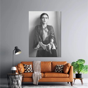 May include: Black and white portrait of a person holding a gun, wearing jewelry and a dark top. The image is a print, likely a photograph, and is displayed on a wall above a brown leather sofa. The room has a modern aesthetic.