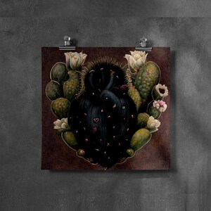 May include: A square print featuring a heart-shaped cactus with a dark, textured center and green, oval-shaped segments. The cactus is adorned with white and pink flowers. The print is attached to a dark brown background with silver clips.