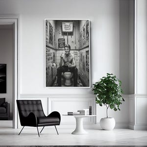 Peut inclure: Impression en noir et blanc d'un homme assis sur des toilettes, entour&eacute; d'affiches. La pi&egrave;ce est lumineuse, avec une chaise noire et une petite table. Une plante en pot et une fen&ecirc;tre sont visibles.