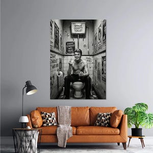 Peut inclure: Impression d'art murale en noir et blanc repr&eacute;sentant une personne assise sur des toilettes dans une salle de bain. Les murs sont couverts d'affiches et d'enseignes, dont "Space Oddity Toilet" et "Ziggy Stardust Was Here."