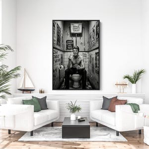 Peut inclure: Impression encadr&eacute;e en noir et blanc d'un homme assis sur des toilettes dans une salle de bain. Les murs sont couverts d'affiches et de panneaux, dont un indiquant "Space Oddity Toilet".