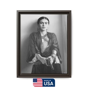 May include: Black and white framed print of a woman in a dark top, skirt, and jewelry, holding a gun. The print is in a dark brown frame. The image includes the text "MADE IN USA" with the American flag.