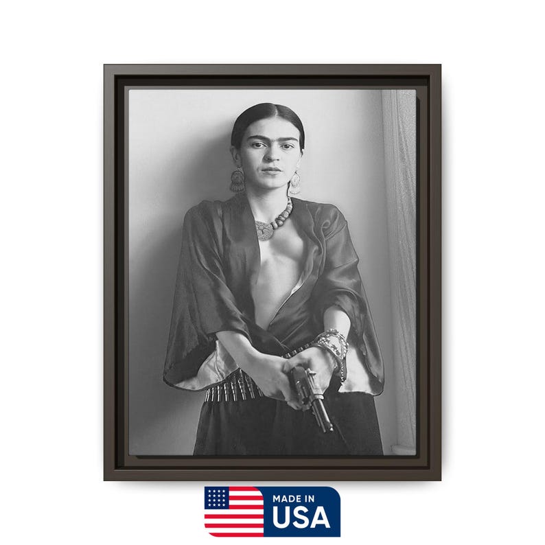 May include: Black and white framed print of a woman in a dark top, skirt, and jewelry, holding a gun. The print is in a dark brown frame. The image includes the text "MADE IN USA" with the American flag.