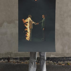 Puede incluir: Un p&oacute;ster con dos figuras con trajes estrech&aacute;ndose la mano sobre un fondo oscuro. Una figura est&aacute; en llamas. El p&oacute;ster lo sostiene una persona con vaqueros y zapatillas, de pie sobre asfalto.