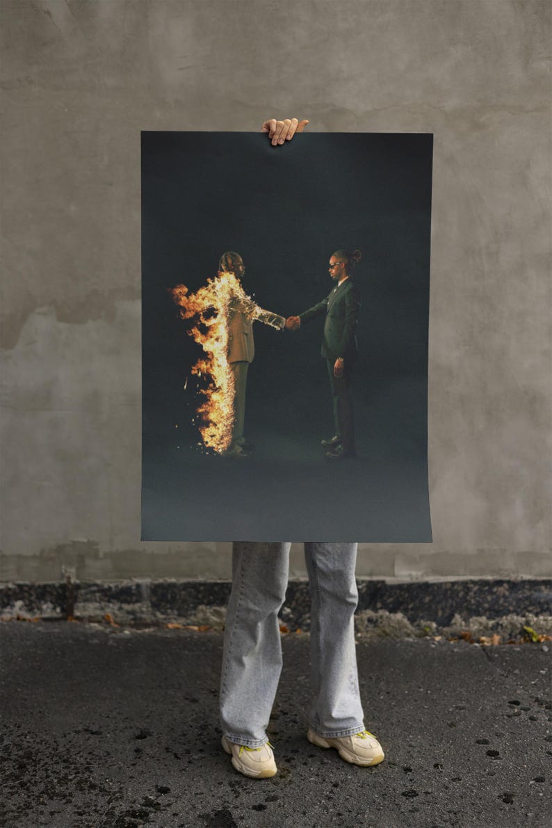 Puede incluir: Un p&oacute;ster con dos figuras con trajes estrech&aacute;ndose la mano sobre un fondo oscuro. Una figura est&aacute; en llamas. El p&oacute;ster lo sostiene una persona con vaqueros y zapatillas, de pie sobre asfalto.