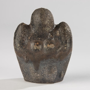 Op de afbeelding: Een donkerbruine keramische sculptuur met een getextureerd oppervlak. De sculptuur heeft een afgeronde bovenkant en twee zijdelingse uitsteeksels, met een donkerder glazuur dat langs de zijkanten druipt. De basis is een lichtere bruintint.