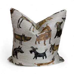 Puede incluir: Cojín decorativo cuadrado con un patrón repetido de perros en tonos marrón, negro y dorado sobre un fondo gris claro. El cojín tiene una textura y está diseñado para la decoración del hogar.