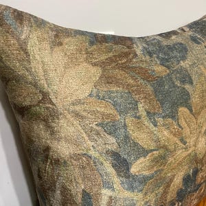 K&ouml;nnte beinhalten: Ein dekoratives Kissen mit einem floralen Muster in Braun-, Beige- und Blaut&ouml;nen. Der Stoff hat ein strukturiertes Aussehen, wobei das florale Muster die gesamte Oberfl&auml;che bedeckt. Das Kissen ist wahrscheinlich aus einem weichen Material gefertigt.