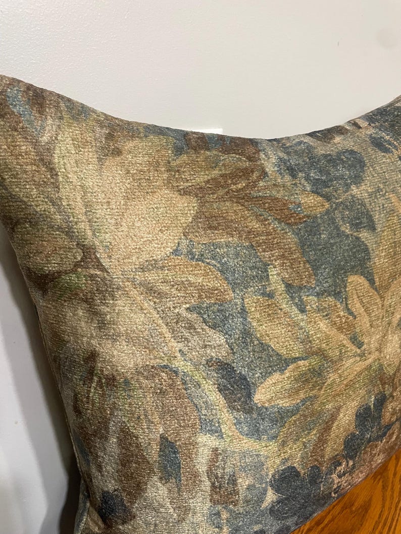 K&ouml;nnte beinhalten: Ein dekoratives Kissen mit einem floralen Muster in Braun-, Beige- und Blaut&ouml;nen. Der Stoff hat ein strukturiertes Aussehen, wobei das florale Muster die gesamte Oberfl&auml;che bedeckt. Das Kissen ist wahrscheinlich aus einem weichen Material gefertigt.