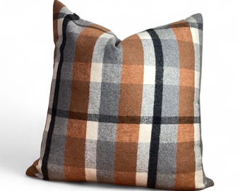 May include: A square cushion with a plaid design. The cushion displays a repeating pattern of brown, grey, black, and white squares. The cushion is made of a soft, textured fabric and is designed for home decor.