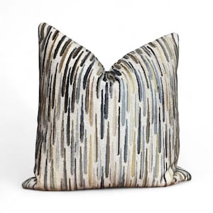 Puede incluir: Cojín decorativo con un patrón de rayas verticales en tonos beige, marrón, azul y verde oliva. La almohada tiene un aspecto suave y texturizado y está diseñada para la decoración del hogar.