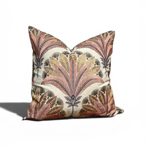 May include: Square cushion with a botanical design. The cream-coloured fabric is patterned with symmetrical pink, brown, and gold stylized plant elements. The cushion has a soft, textured appearance and would suit a living room.