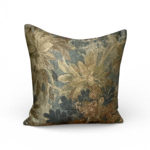 K&ouml;nnte beinhalten: Quadratisches Zierkissen mit floralem Muster in Gold-, Braun- und Blaugr&uuml;nt&ouml;nen. Der Stoff wirkt strukturiert, mit einem Design aus stilisierten Bl&auml;ttern und Blumen. F&uuml;r Sofa oder Bett geeignet.