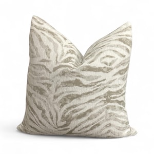 May include: A decorative pillow with a zebra stripe pattern. The pillow features a neutral color palette with beige and light brown stripes. The pillow is square and has a soft, textured appearance.