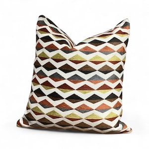 May include: A square cushion with a geometric diamond pattern. The cushion displays a repeating pattern of diamonds in shades of brown, orange, grey, and gold on a white background. The cushion has a soft, textured appearance and is designed for decorative use.