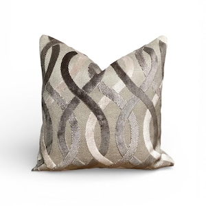 May include: Decorative square pillow with a woven texture and an abstract pattern of interlocking loops in shades of gray, beige, and brown. The pillow has a soft, plush appearance and is designed for home decor.