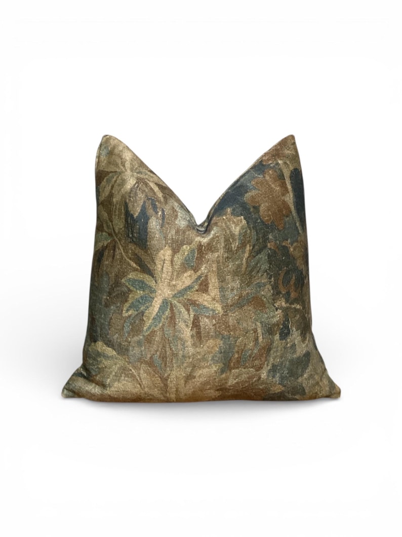 K&ouml;nnte beinhalten: Ein dekoratives Zierkissen mit einem botanischen Muster. Das Kissen hat ein tapisserieartiges Design mit Braunt&ouml;nen, Gr&uuml;n und Blau. Das florale Muster ist detailliert und bedeckt die gesamte Oberfl&auml;che des Kissens, wodurch ein strukturiertes Aussehen entsteht.