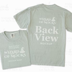 May include: Two light green t-shirts, one folded and one displayed with the back facing up. The folded shirt has the text "WIZARD OF MOCKS MOCKUP SHOP" and "Real Product Photography". The back of the other shirt reads "Back View MOCKUP" and "WIZARD OF MOCKS".