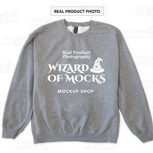May include: A heather gray crewneck sweatshirt featuring white screen-printed text that reads Real Product Photography WIZARD OF MOCKS MOCKUP SHOP with a small graphic of a wizard hat with stars above the word WIZARD.