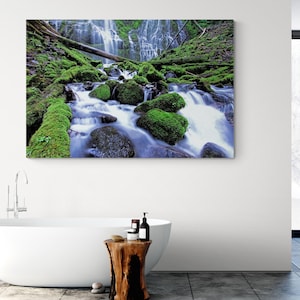 Può includere: Una stampa su tela di una scena di cascata. L'immagine presenta una cascata a cascata con acqua che scorre su rocce e tronchi coperti di muschio. La scena è dominata da sfumature di verde e blu.